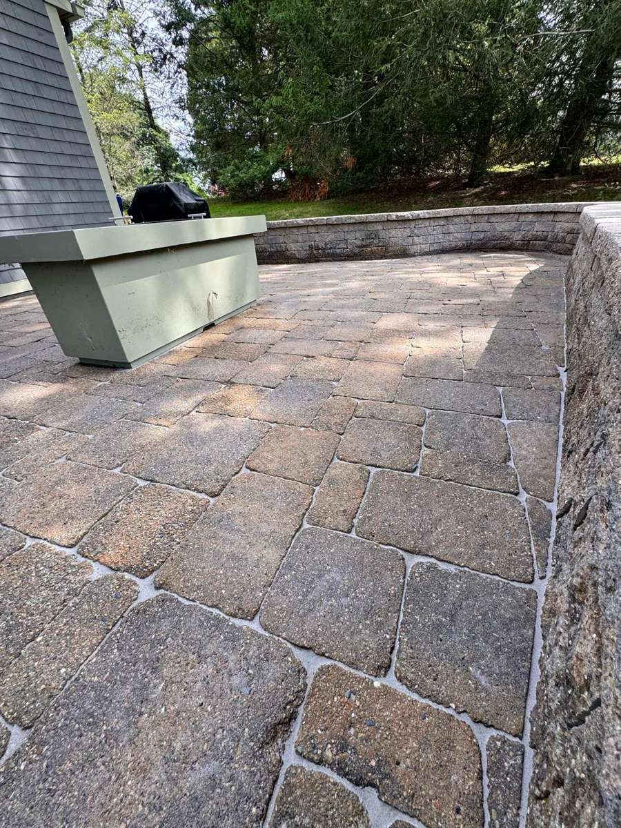 Tan and brown cobblestone paver patio with retaining wall and fresh polymeric sand joints
